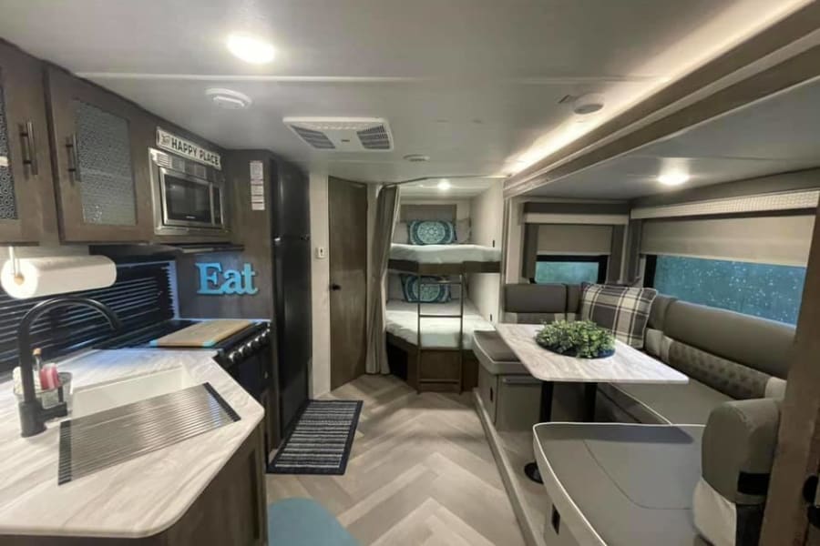 This RV rental interior features a modern kitchen, comfortable dining area, and cozy bunk beds.