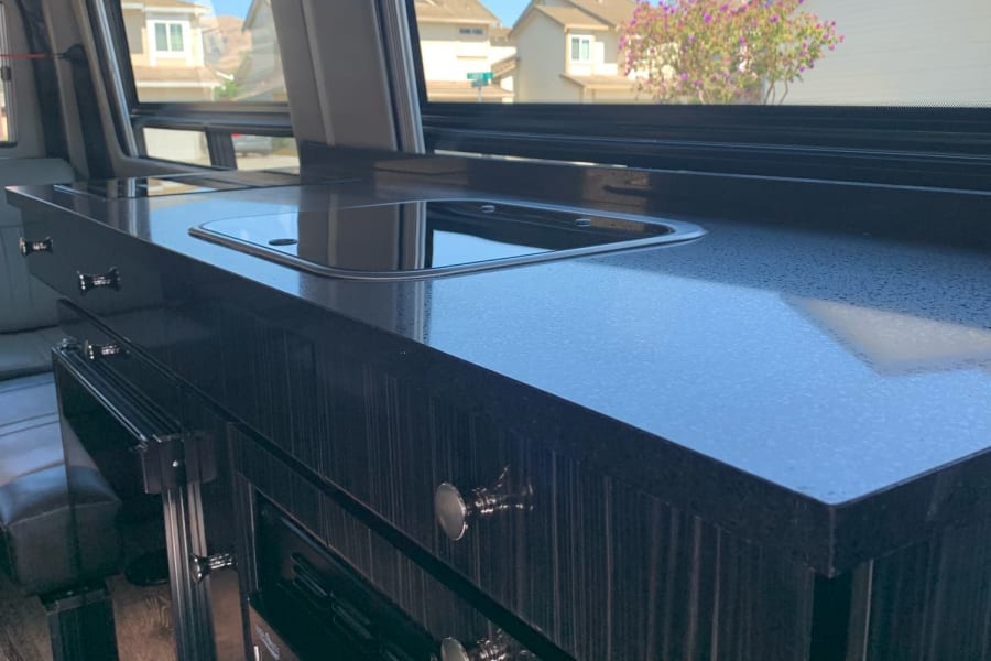 Sleek RV rental interior features a dark kitchen countertop with a sink, modern cabinets, and a scenic window view.