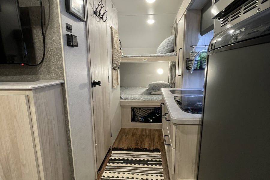 Inside an rv rental: a cozy hallway with bunk beds, a compact kitchen, and a patterned rug on wood flooring.