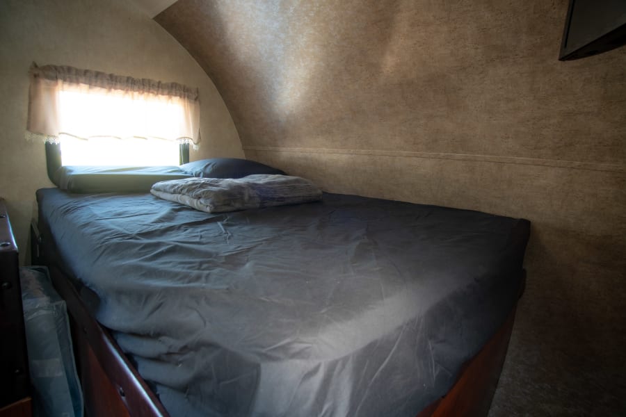 Cozy RV rental bedroom with a bed, pillow, and blanket by a bright window. A comfortable travel lodging option.