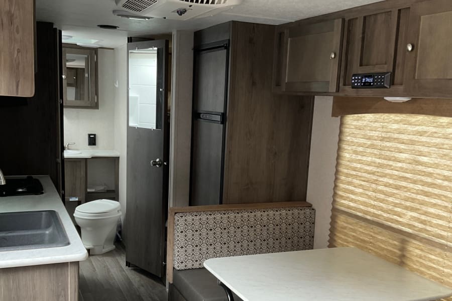 Spacious RV rental interior featuring a compact kitchen, bathroom, refrigerator, and comfortable dinette area.