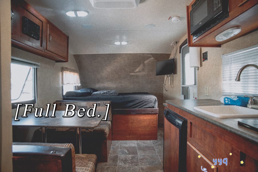RV rental interior featuring a full bed, dinette, and well-equipped kitchen. Ideal for a comfortable travel trailer stay.