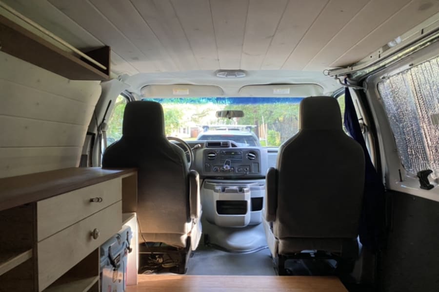 Step inside this RV rental's camper van interior. Features include wooden paneling, a cabinet, and front seats, ready for adventure.