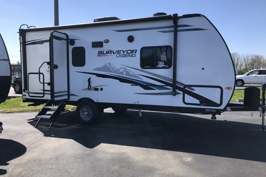 A sleek white Forest River Surveyor Legend travel trailer, perfect for your next RV rental adventure, parked outdoors.