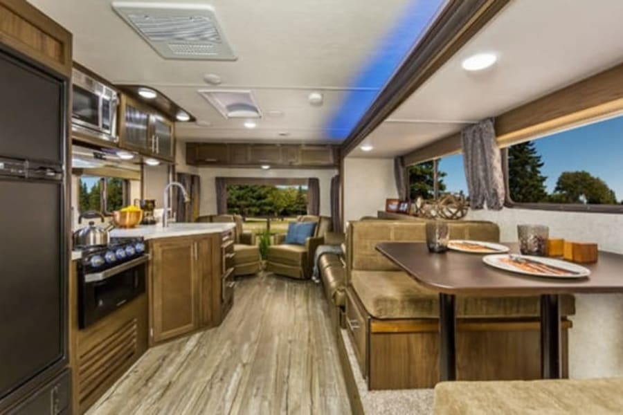 Explore this modern RV rental's inviting interior, showcasing a full kitchen, dining booth, and comfortable living space.