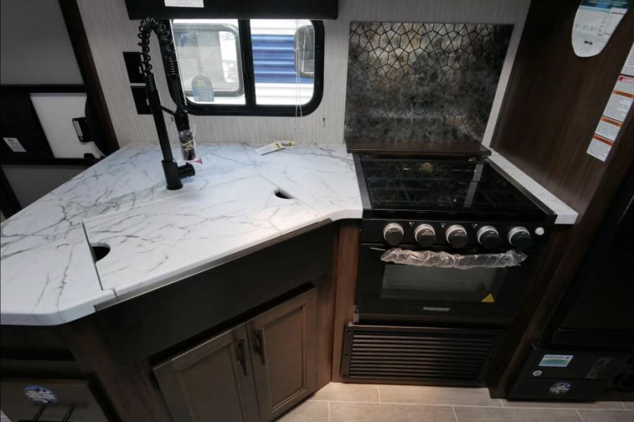 Modern RV rental kitchen featuring white marble-look counters, black faucet, built-in stove/oven, and a stylish geometric backsplash.