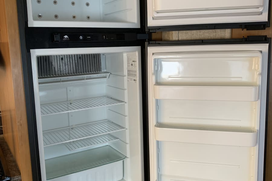 Empty two-door RV rental refrigerator, ready for your trip. Clean shelves and door bins are visible inside.