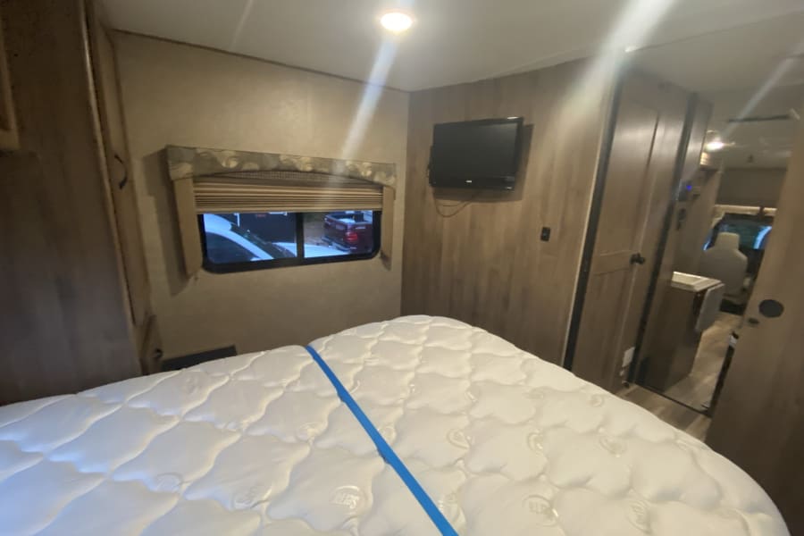 RV rental bedroom with a fresh Serta mattress, wall-mounted TV, and window views. Cozy interior space.