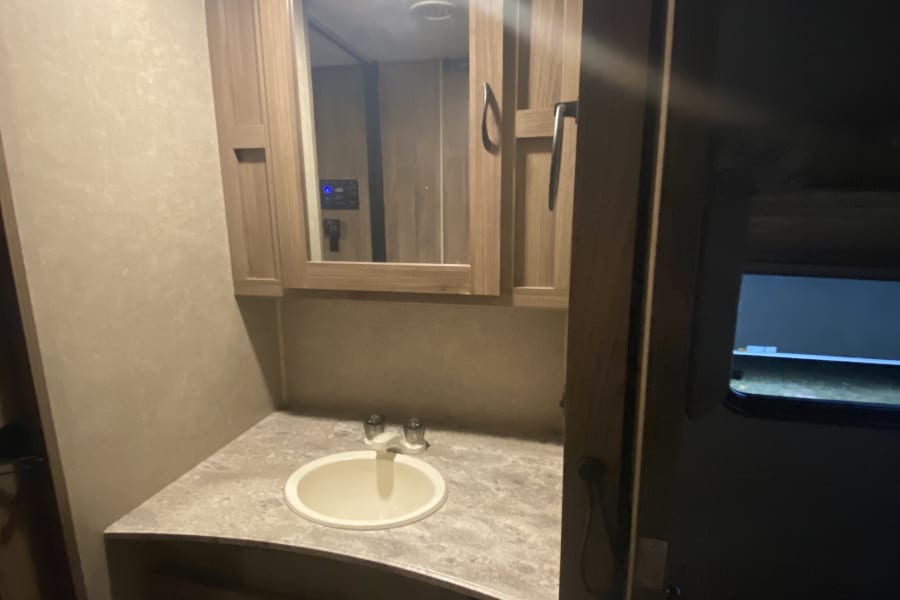 Inside an RV rental: a compact bathroom vanity with a sink, mirror, and cabinets, ideal for road trips.