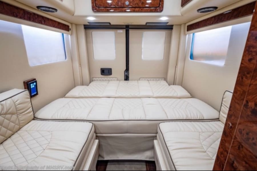 Experience comfort in this rv rental. The luxury van interior features two quilted beige beds/benches and wood trim.