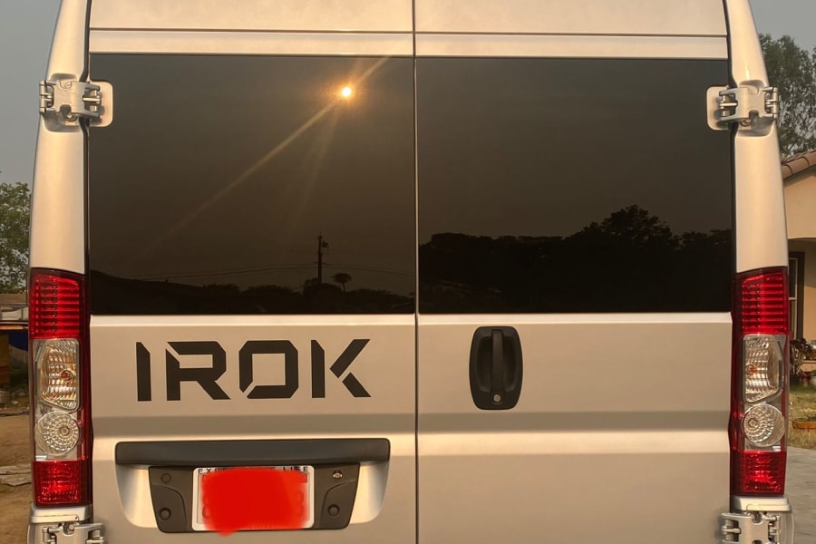 Silver IROK RV rental's rear view: dual doors, dark tinted windows, top camera, & antenna.