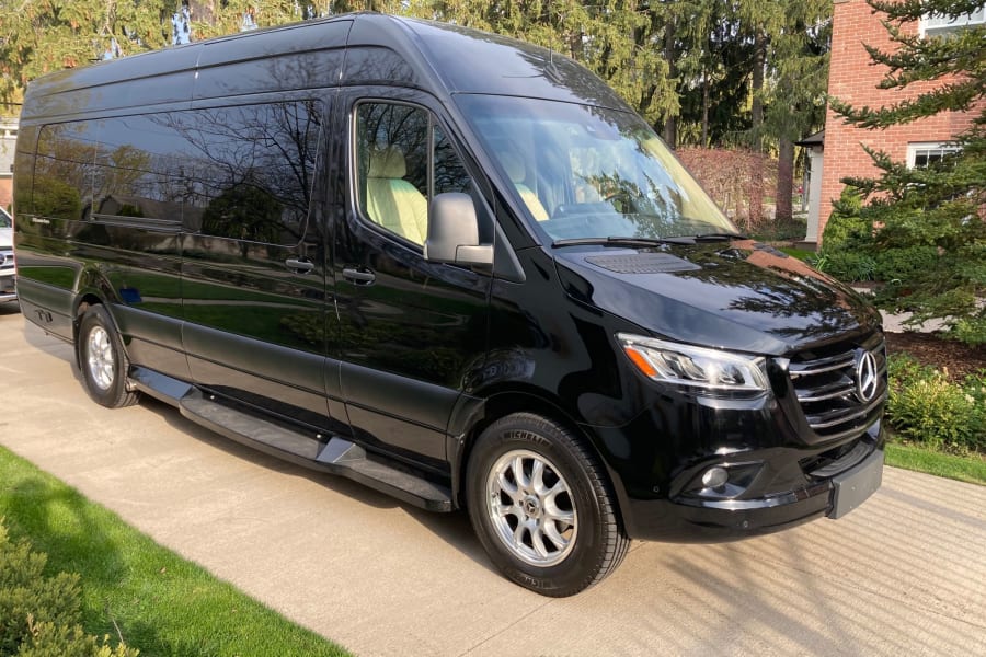 A black Mercedes-Benz Sprinter van, a luxurious RV rental option, with tinted windows, parked on a paved driveway.
