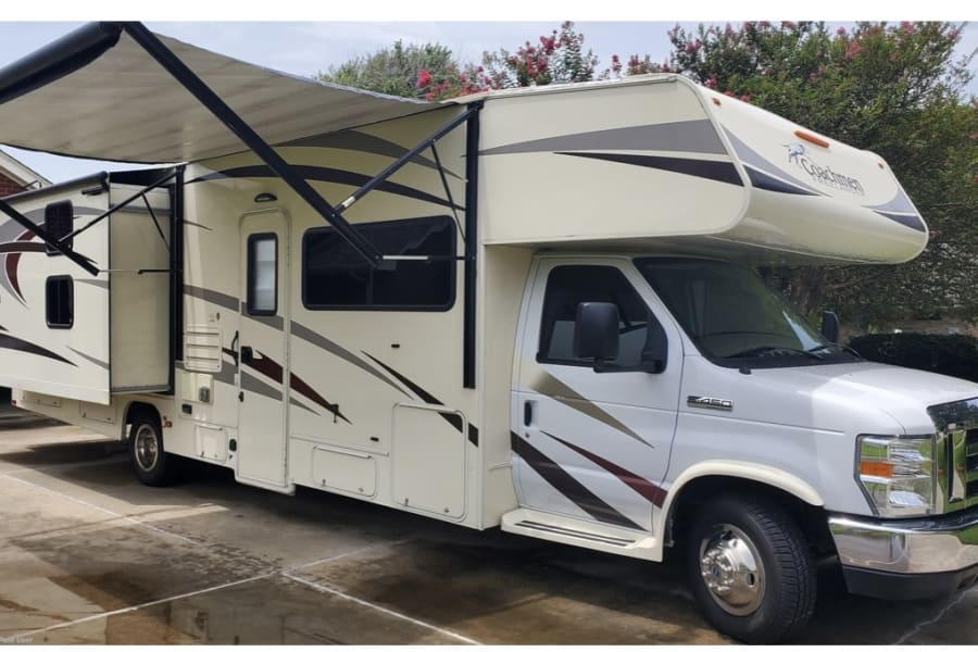 White and tan Class C motorhome RV rental, featuring an extended awning and slide-out. Perfect for your next adventure.