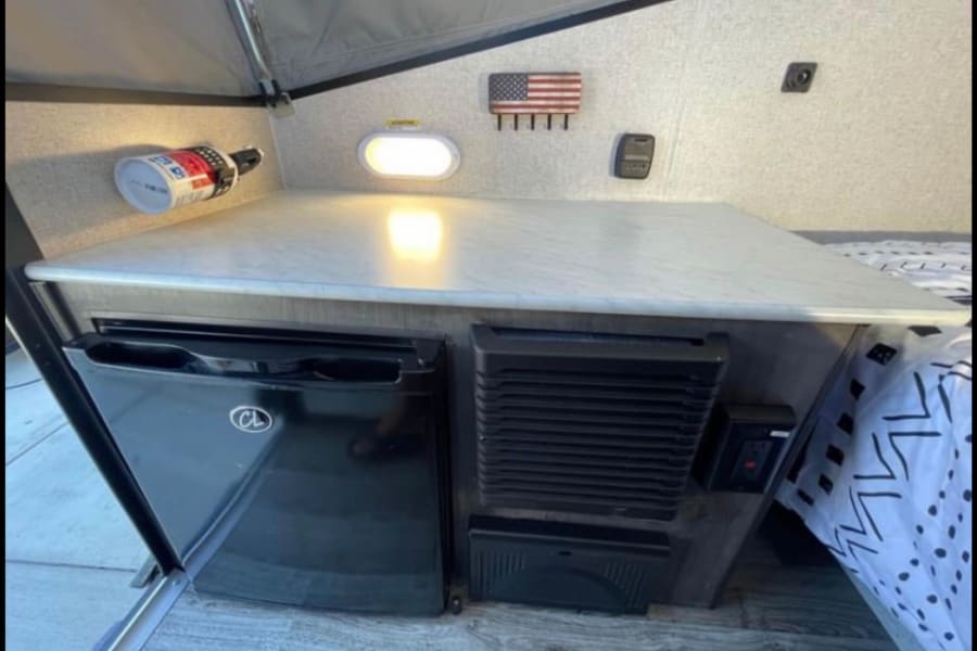 Explore this RV rental's efficient interior: counter, fridge, safety gear, and cozy sleeping area.