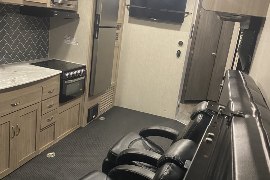 Inside an **rv rental**: full kitchen, stainless steel fridge, TV, and two cozy recliners for comfort.