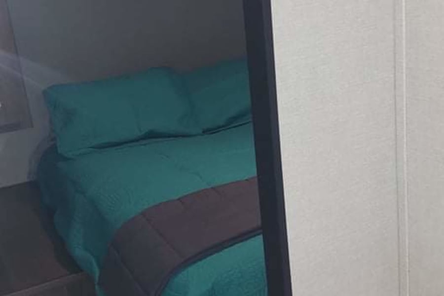 Cozy RV rental bedroom features a teal bed, overhead cabinets, and wood-look flooring.