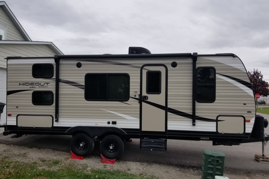 This light-colored "Hideout LITS" travel trailer, an ideal rv rental, is parked on gravel with red wheel chocks.
