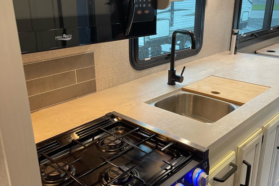 Modern RV rental kitchen featuring a High Pointe microwave, gas stove with blue-lit knobs, and stainless steel sink.
