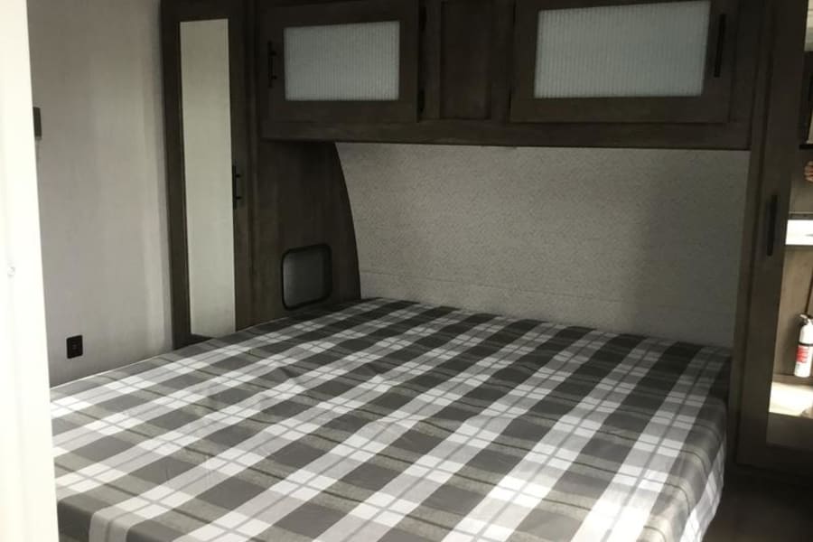 RV rental bedroom featuring a plaid bed, overhead storage, mirrored closet, and a fire extinguisher for safety.