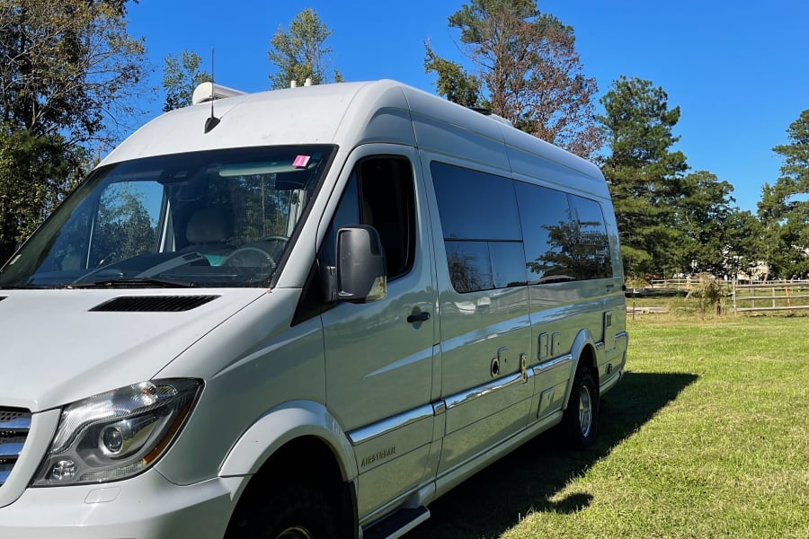 White Mercedes Sprinter Airstream RV rental parked on sunny green grass under a clear blue sky.