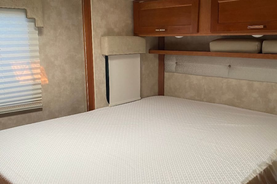 Comfortable RV rental bedroom with a large bed, overhead wood cabinets, window, and skylight.