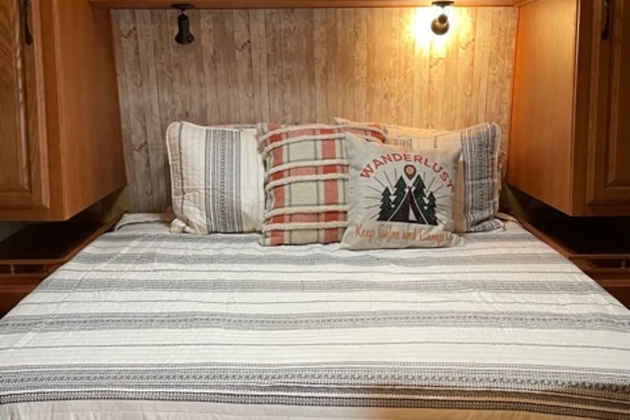 Cozy RV rental bedroom with striped quilt, wanderlust pillow, wood paneling, and built-in cabinets.