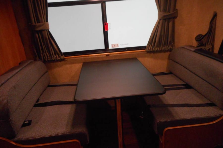 RV rental dinette area: Two cozy benches with a dark table between them, and a window with brown curtains.