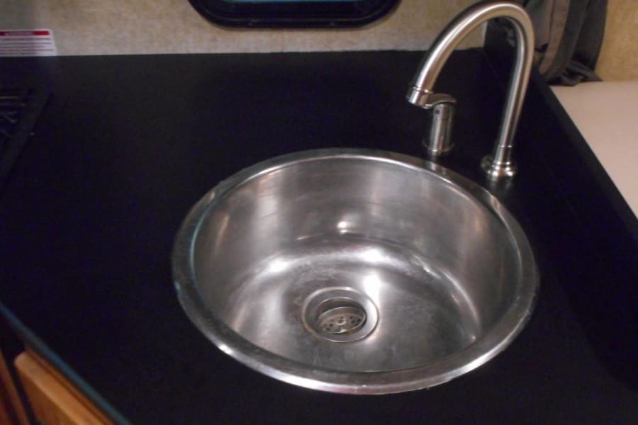 Compact RV rental kitchen sink and faucet on dark countertop. A clean, stainless steel basin for your travels.