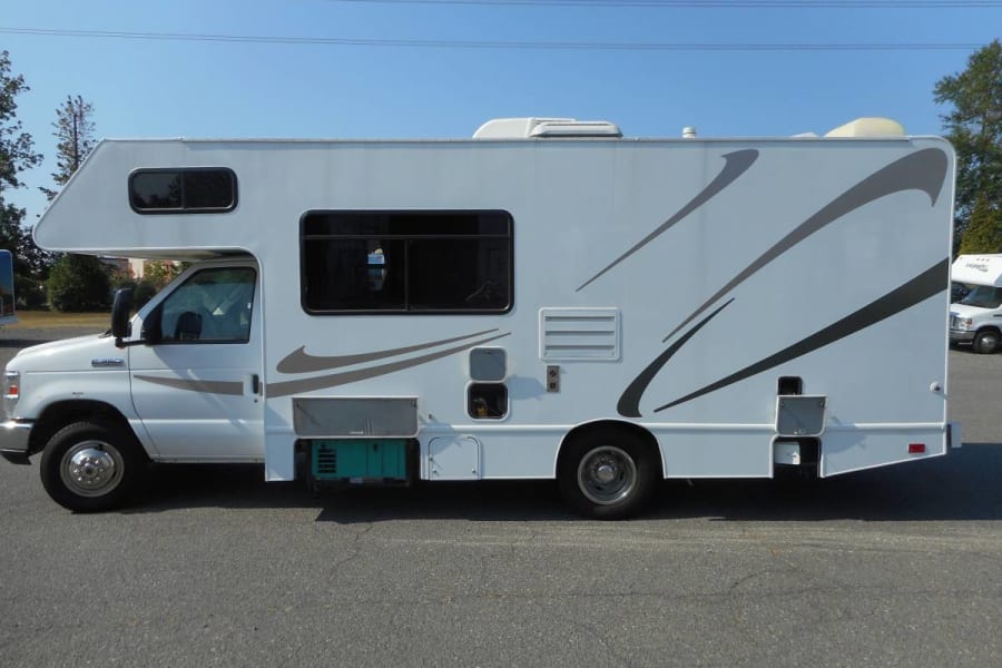 White Class C RV rental with graphics, a motorhome featuring a generator, parked on asphalt. Ideal camper for adventures!
