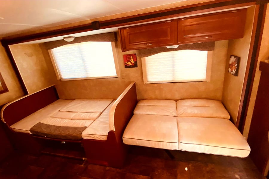 Cozy RV rental interior featuring two convertible dinette beds, windows, and overhead cabinets.