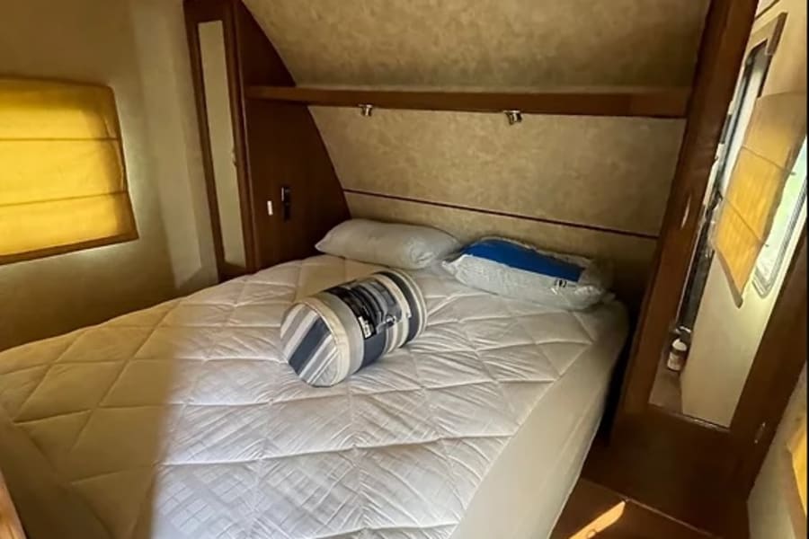 RV rental bedroom interior: a white quilted bed, overhead shelving, and AC unit provide comfort in this compact space.