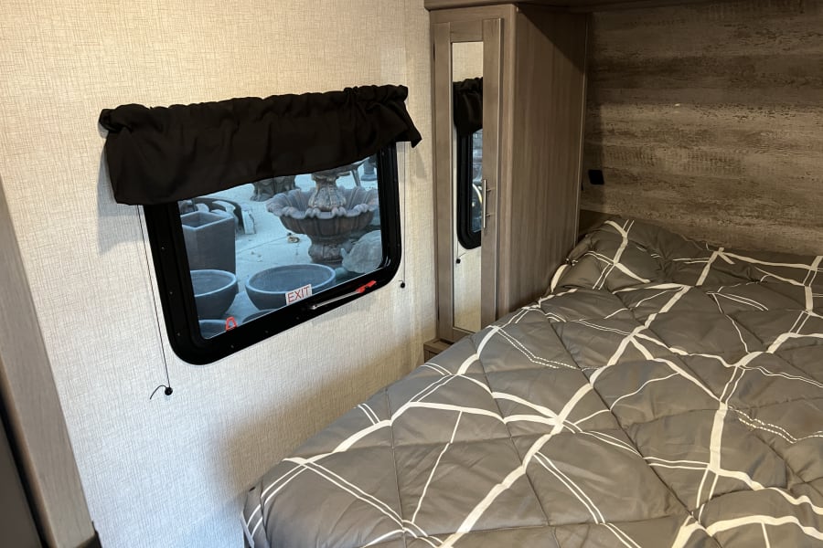 RV rental bedroom featuring a bed with patterned comforter, a window with an 'EXIT' sign, and built-in cabinetry.