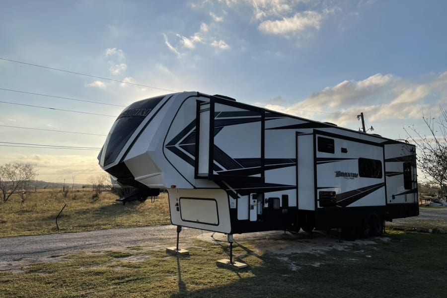A modern, white and black fifth-wheel recreational vehicle, an ideal rv rental, parked in a sunny, open field.