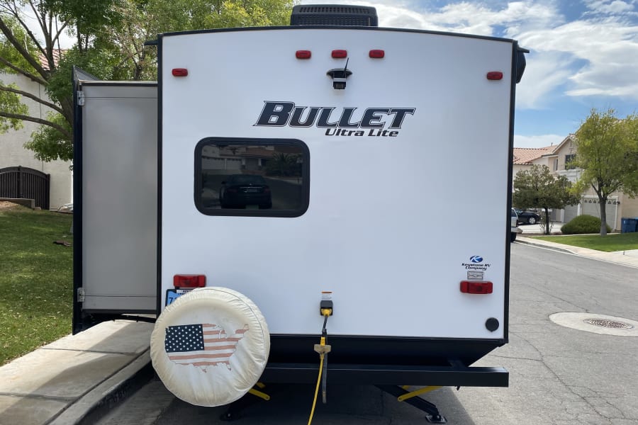 Bullet Ultra Lite travel trailer parked for an rv rental, featuring a US flag spare tire cover and power hookup.