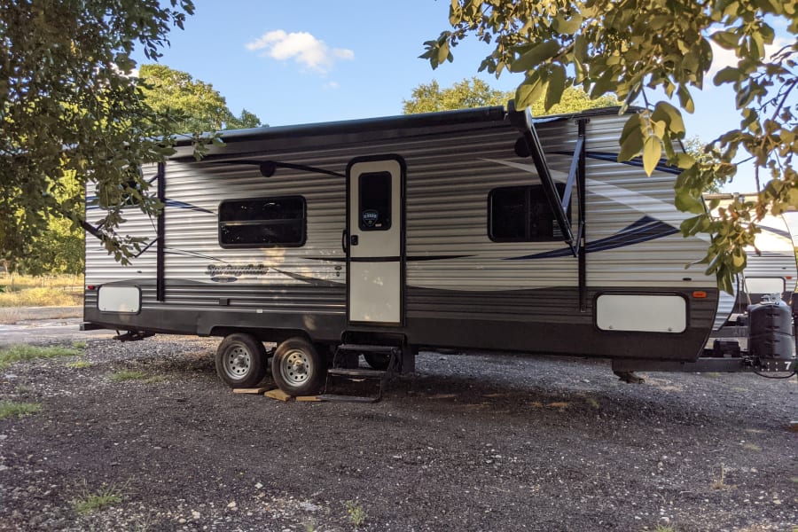 Springdale travel trailer RV rental with extended awning, parked on gravel. Perfect for a relaxing getaway!