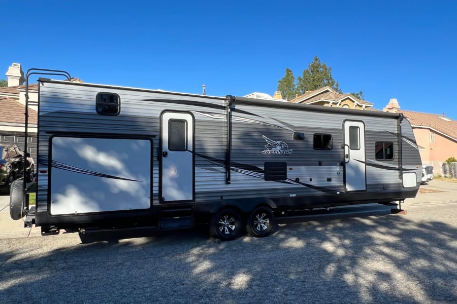 A sleek grey Jay Flight travel trailer, an excellent RV rental option, parked on a sunny street.