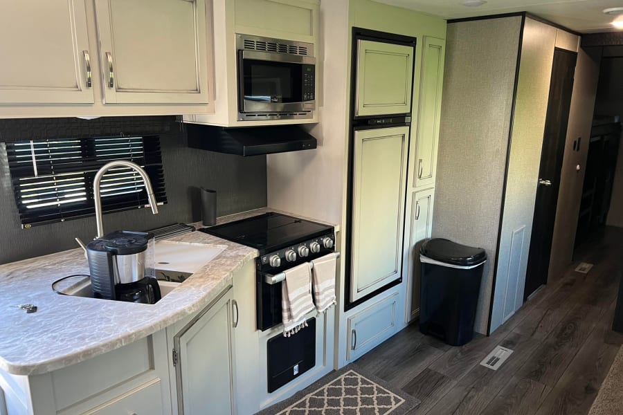 This RV rental features a modern kitchen area with a sink, microwave, stove, fridge, and ample cabinet space, perfect for travel.