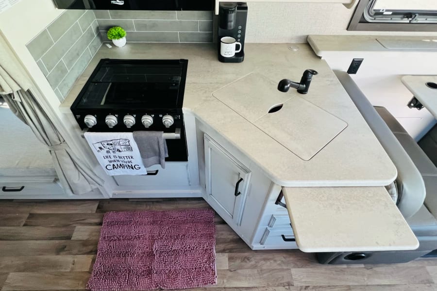A well-equipped RV rental kitchen featuring a stove, sink, coffee maker, and practical extendable counter space.