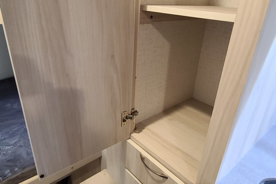 RV rental interior: Light wood cabinetry with open shelving, two drawers, and a bunk area for compact living.