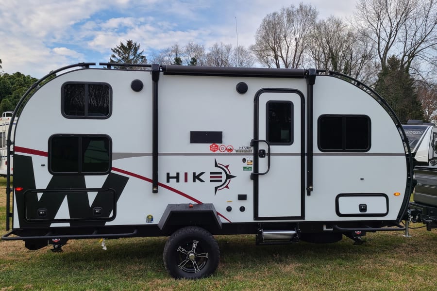 A white Winnebago Hike travel trailer, ideal for an rv rental, parked on grass & hooked to a truck.