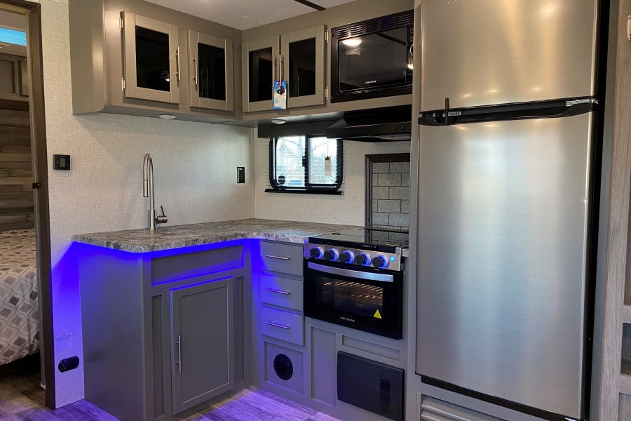 Inside a modern RV rental: sleek kitchen with stainless steel appliances, sink, and cool blue under-counter lighting.