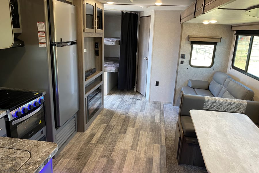Spacious RV rental interior featuring a kitchen with stove/fridge, dining booth, comfy sofa, and private bunk beds.