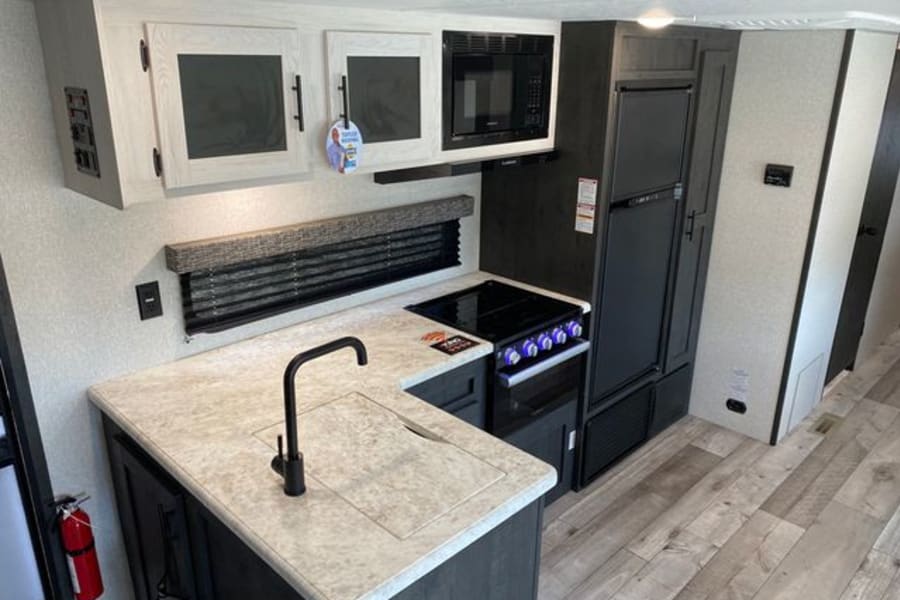 RV rental kitchen: light cabinetry, black appliances (fridge, microwave, stove), sink, & faucet visible.