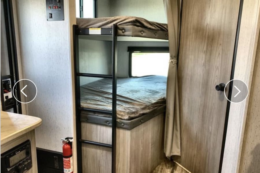 Inside an RV rental, two bunk beds, a control panel, and a red fire extinguisher are clearly visible.