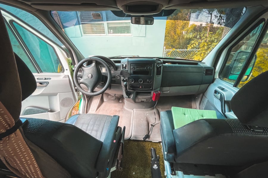 Inside an RV rental camper van, revealing the cockpit, dashboard, and front seats from a rear perspective.