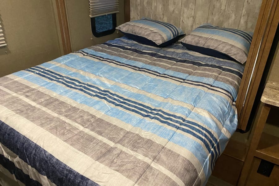 Inside an RV, a cozy bedroom features a striped comforter and pillows, great for an rv rental.