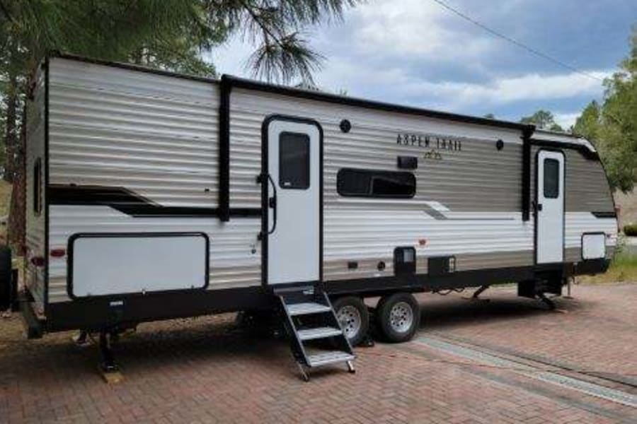 This travel trailer is available for rv rental, featuring two doors, steps, and an awning.