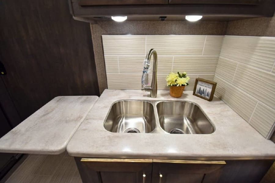 Modern RV rental kitchen with double sink, extendable counter, and stylish backsplash.