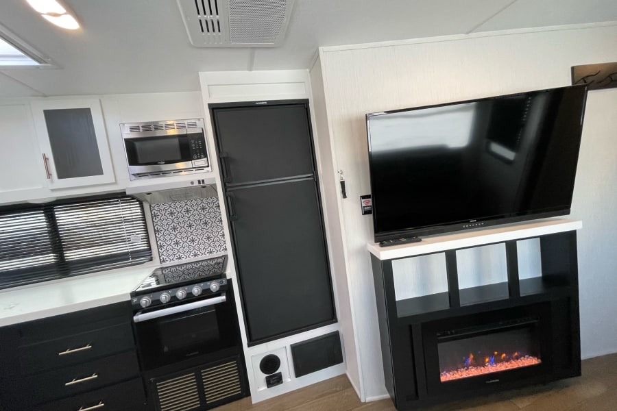 Experience the comfort of this modern RV rental interior featuring a full kitchen, refrigerator, large TV, and electric fireplace.
