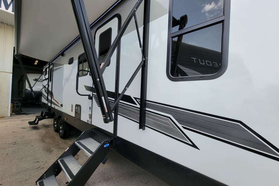 This modern white RV rental showcases its extended awning with LED lights and sturdy deployed steps for easy access.